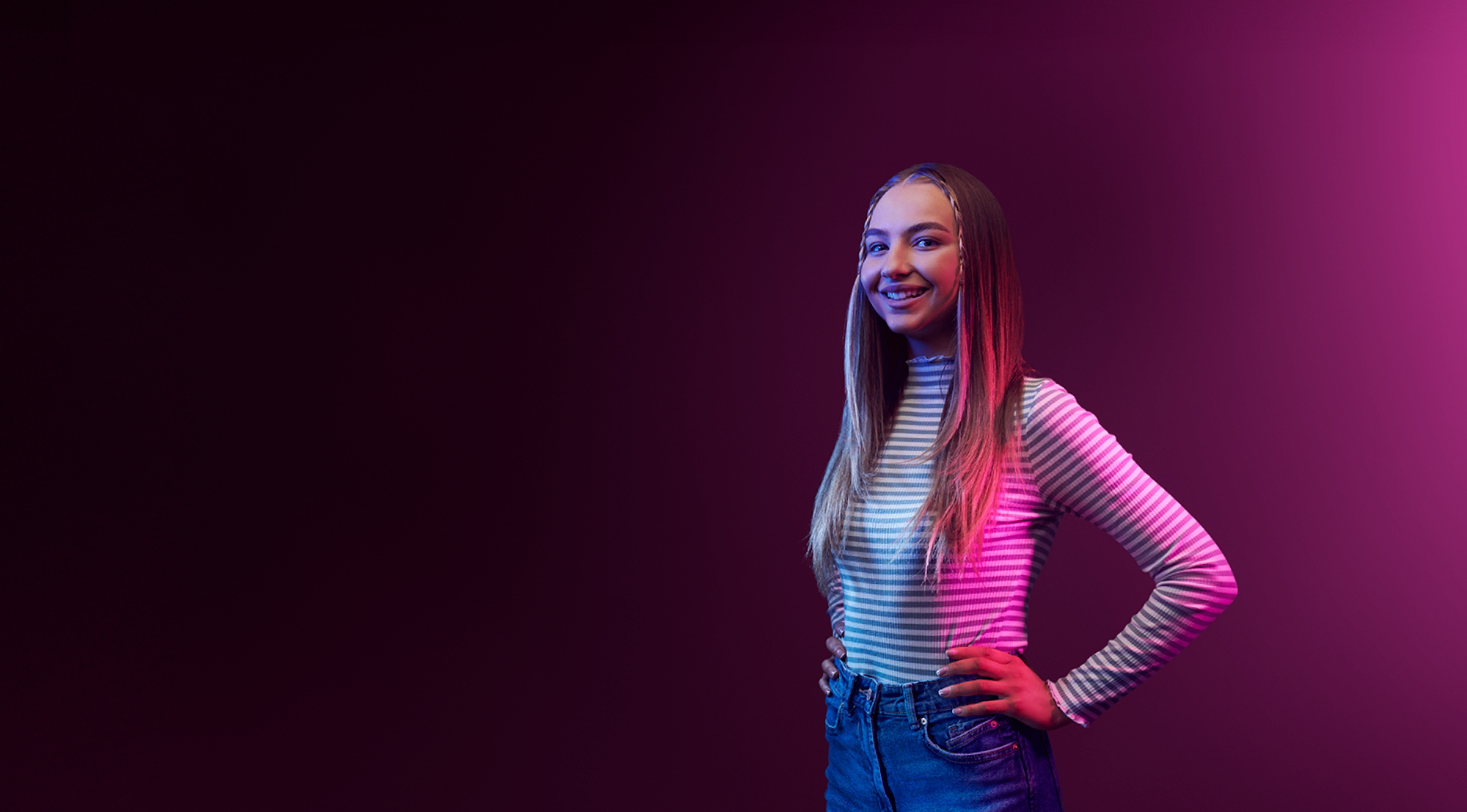 Purple background with student in striped shirt smiling with their hands on their hips