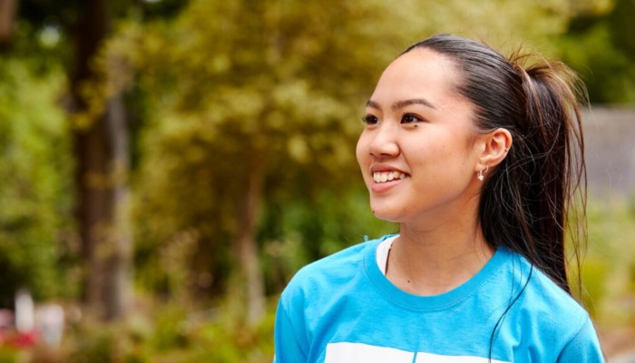 A Sheffield Hallam open day ambassador in a blue t shirt smiling. Trees can be seen in the background.